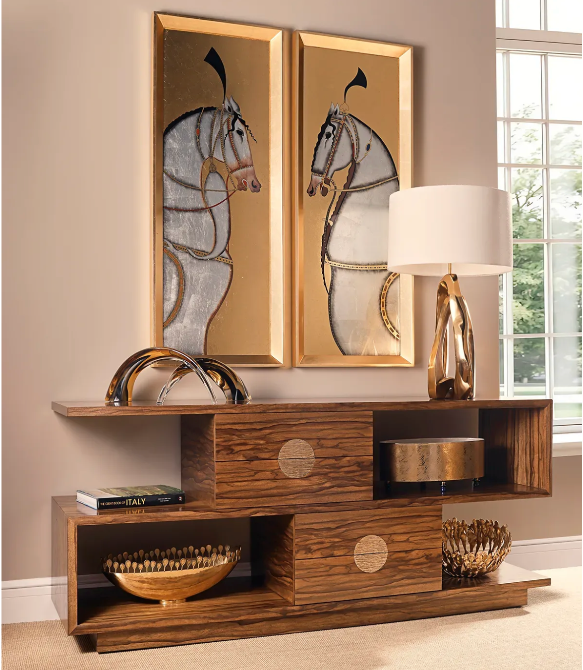 A walnut console table styled with a sculptural brass lamp, gold-leaf equestrian panels above, stacked books, and gilded bowls | Cayen Home, Carmel-by-the-Sea