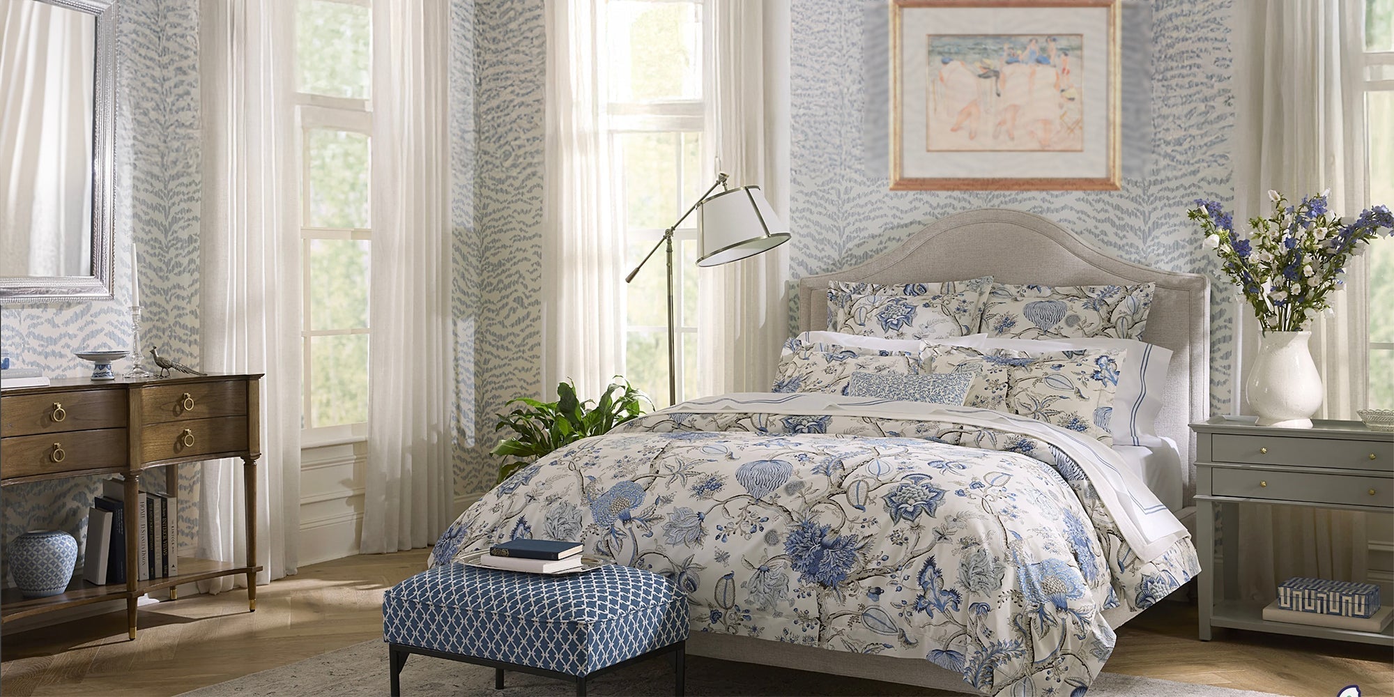 A bed dressed in a blue and white botanical Sferra x Scalamandre linen collection, layered with matching shams and a floral coverlet.