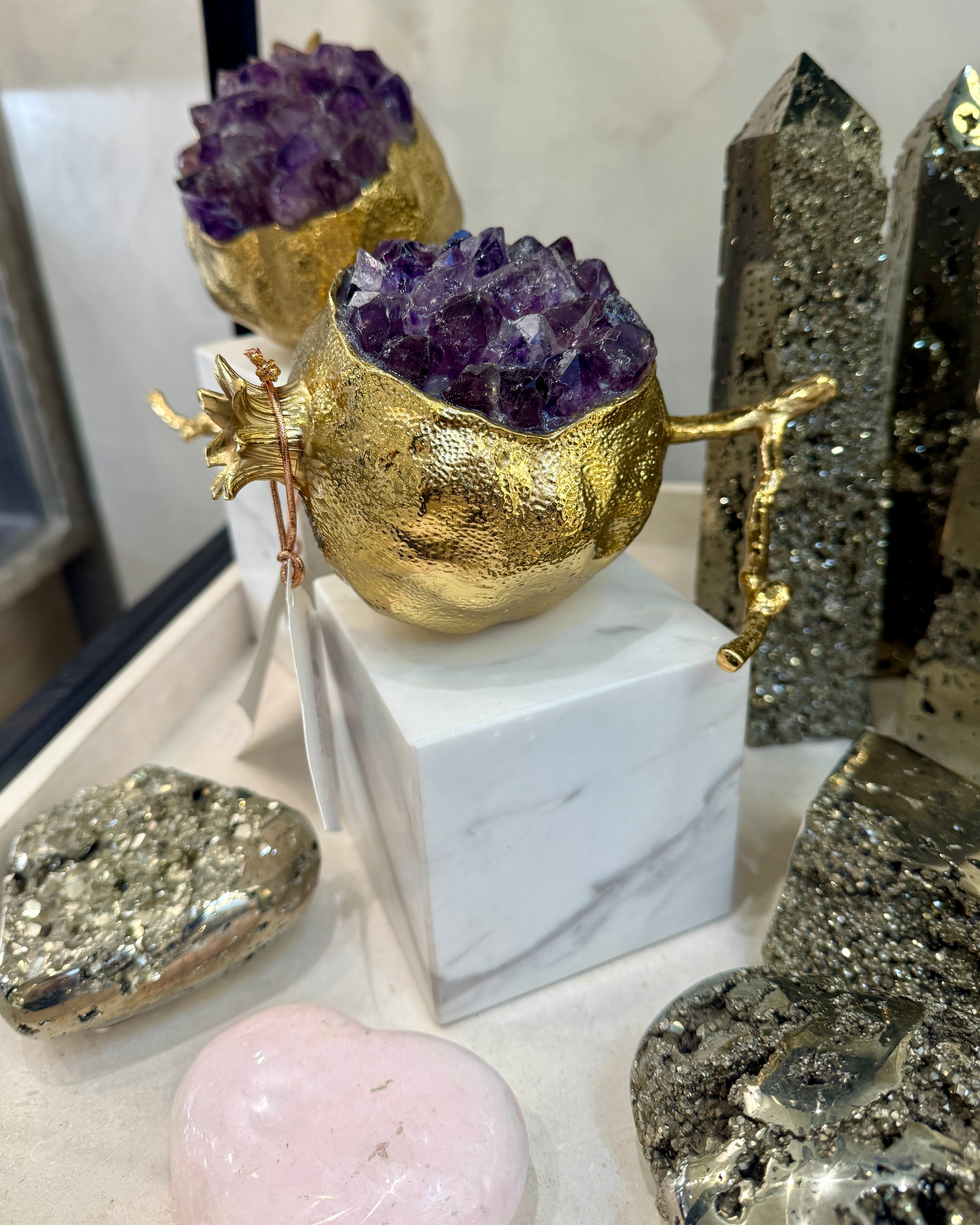 Gold pomegranate vessels filled with amethyst crystals styled on a marble pedestal beside pyrite obelisks at Cayen Home