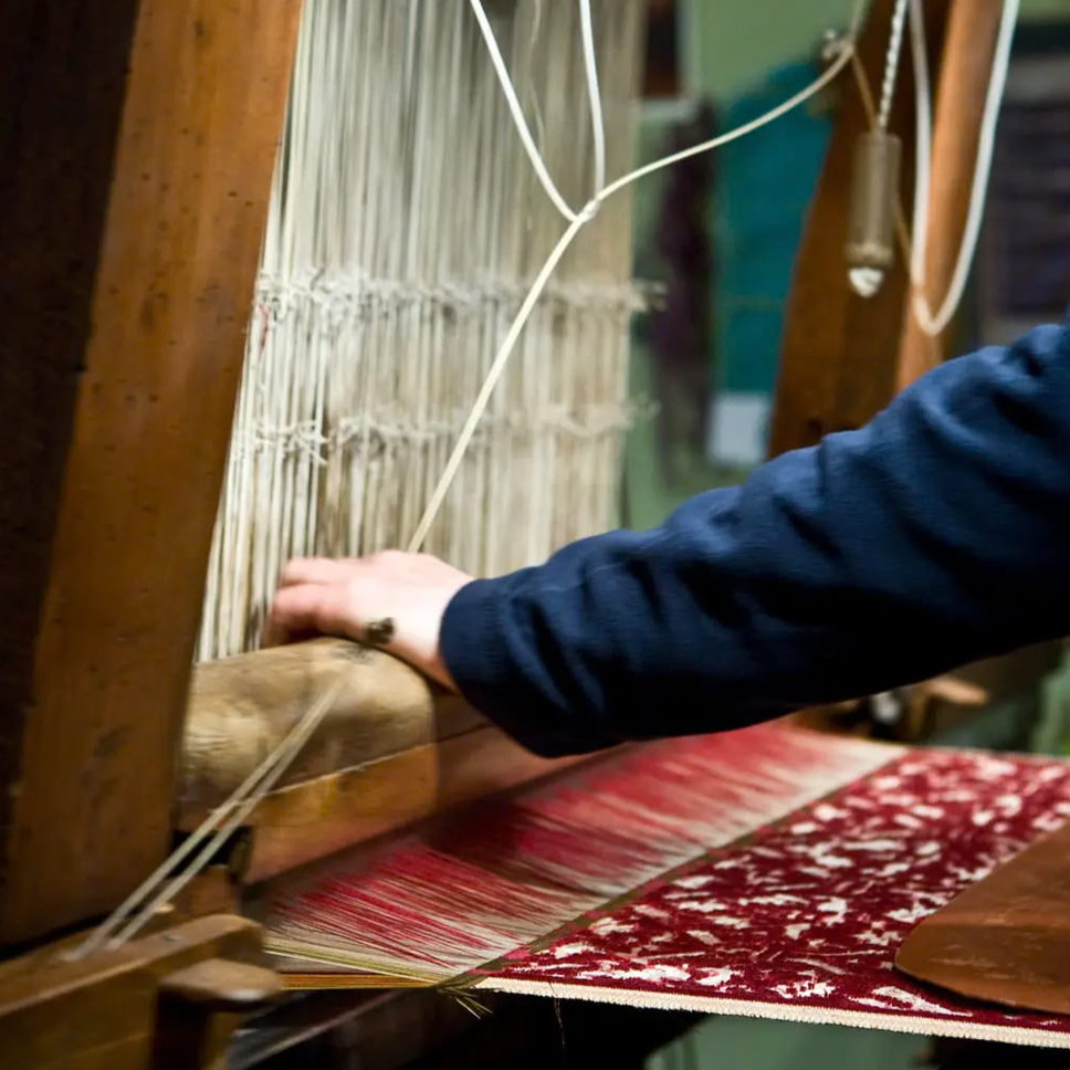 Person weaving on a traditional loom with red and white yarn.